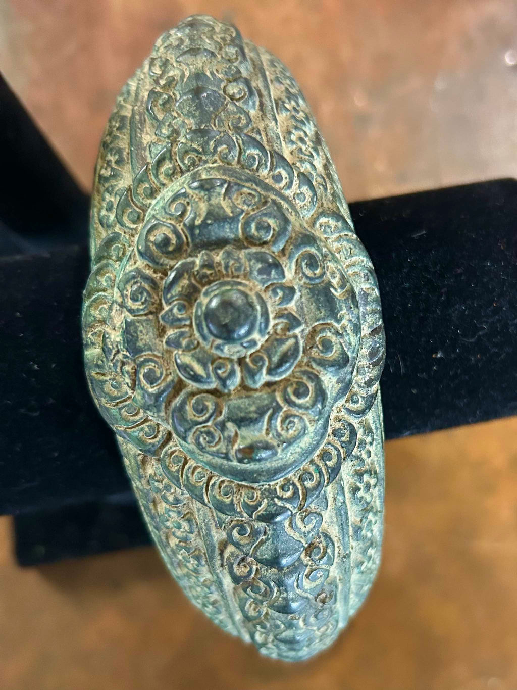 Antique bronze warrior bracelet with intricate patterns on a black stand.