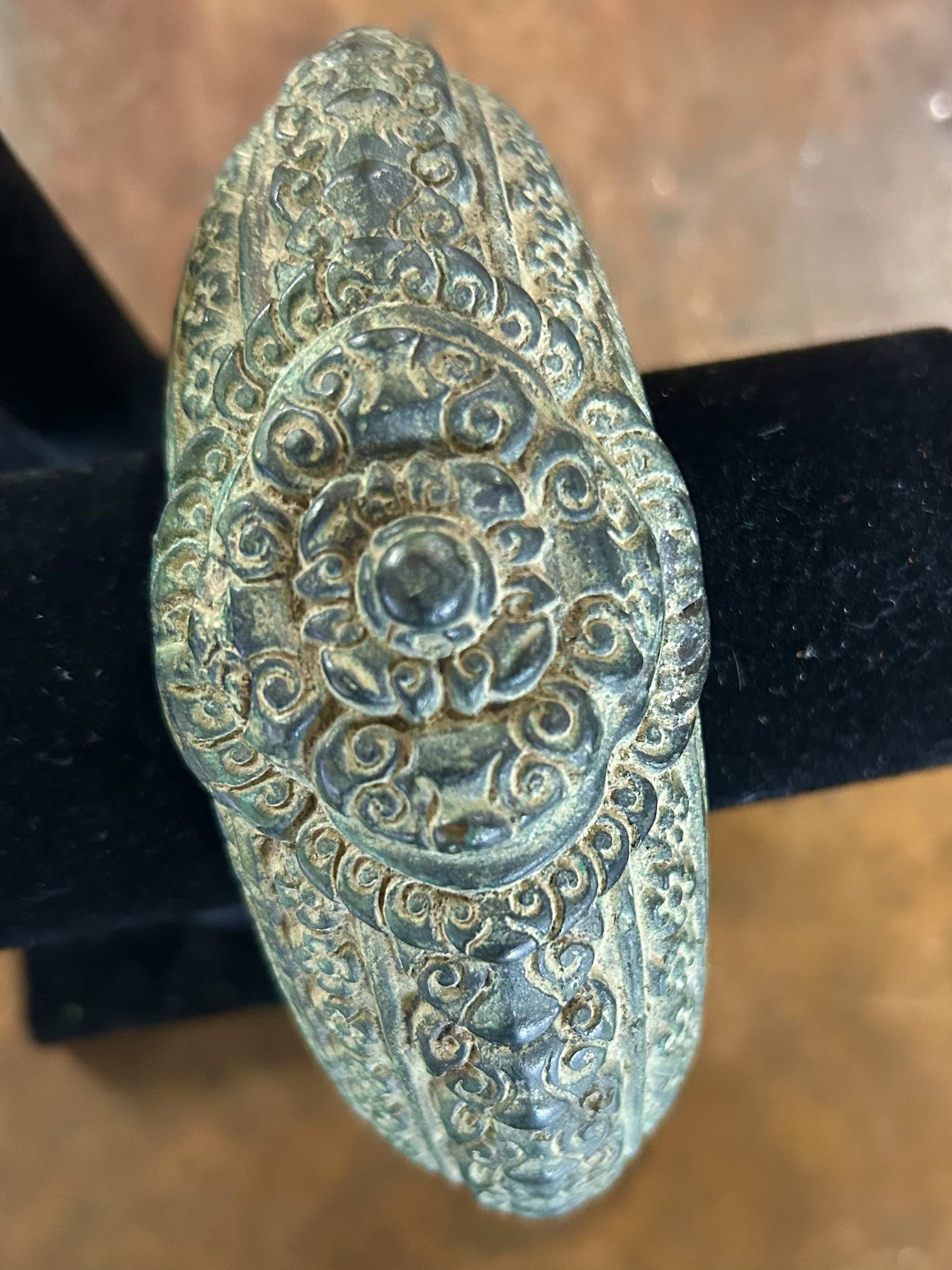 Antique bronze warrior bracelet with intricate patterns on a black stand.