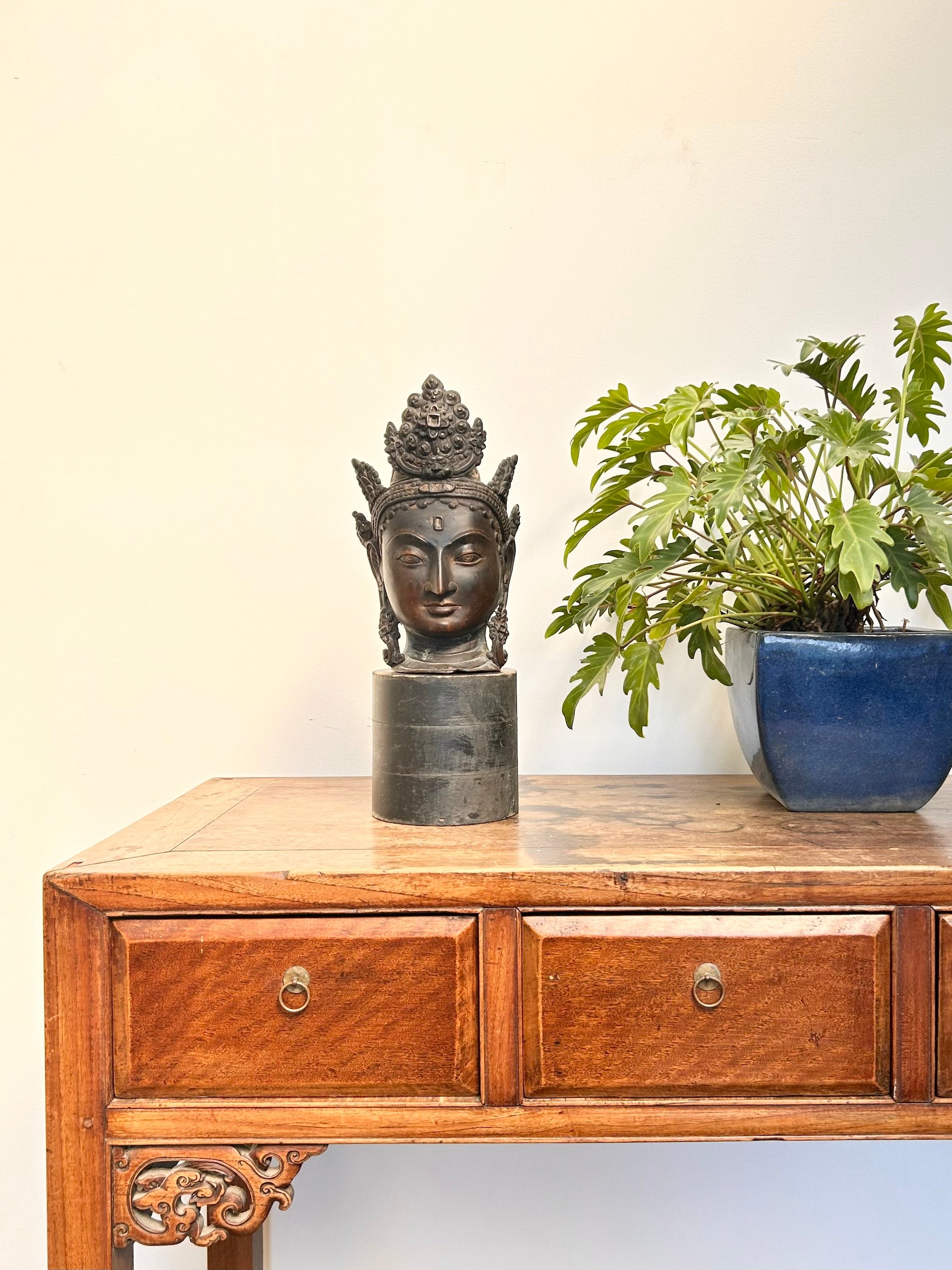Wooden cabinet with a bronze Buddha head sculpture and a potted plant on a light background