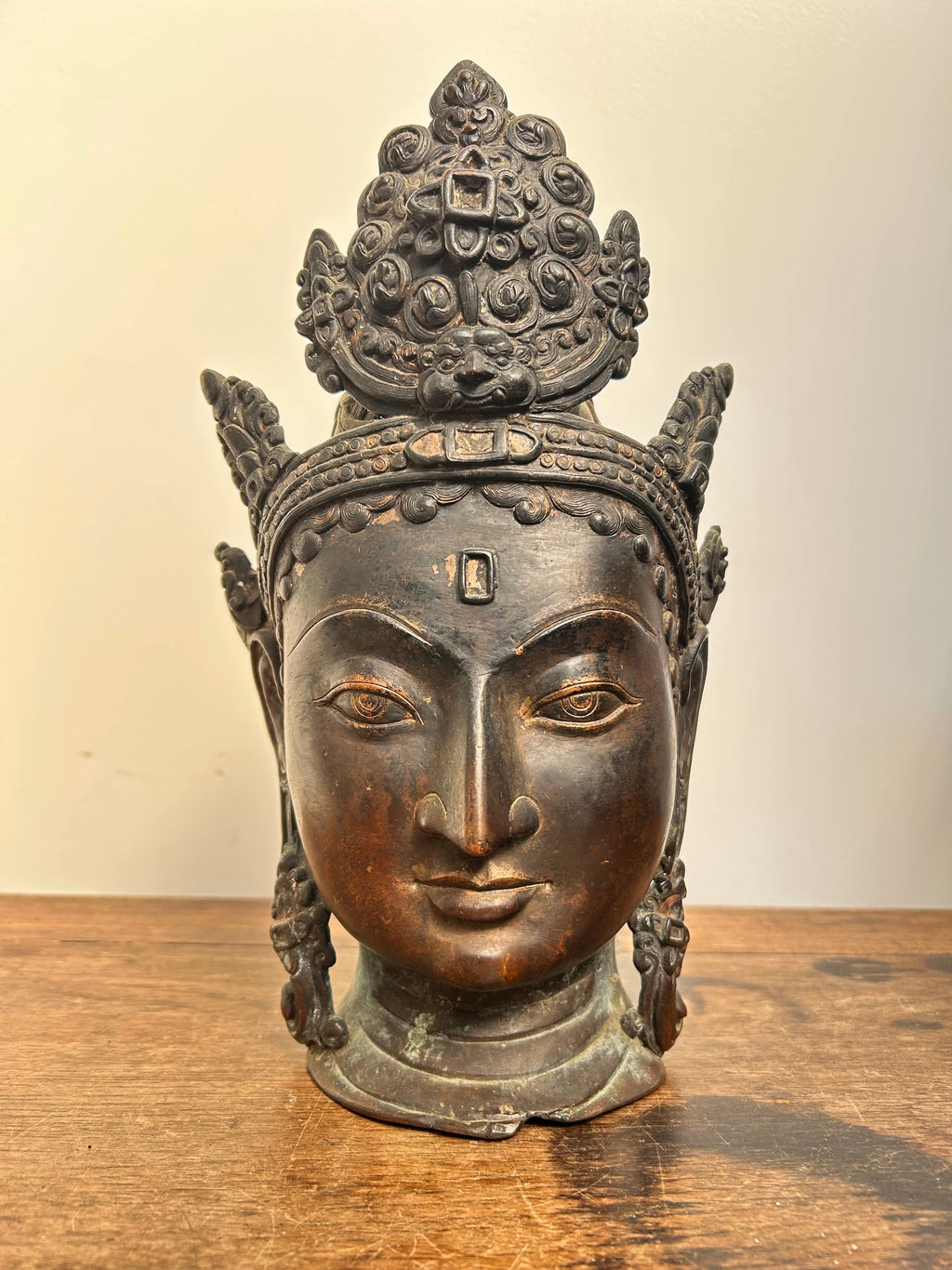 Bronze head sculpture of Tara a deity on a wooden surface with a beige background
