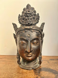 Bronze head sculpture of Tara a deity on a wooden surface with a beige background
