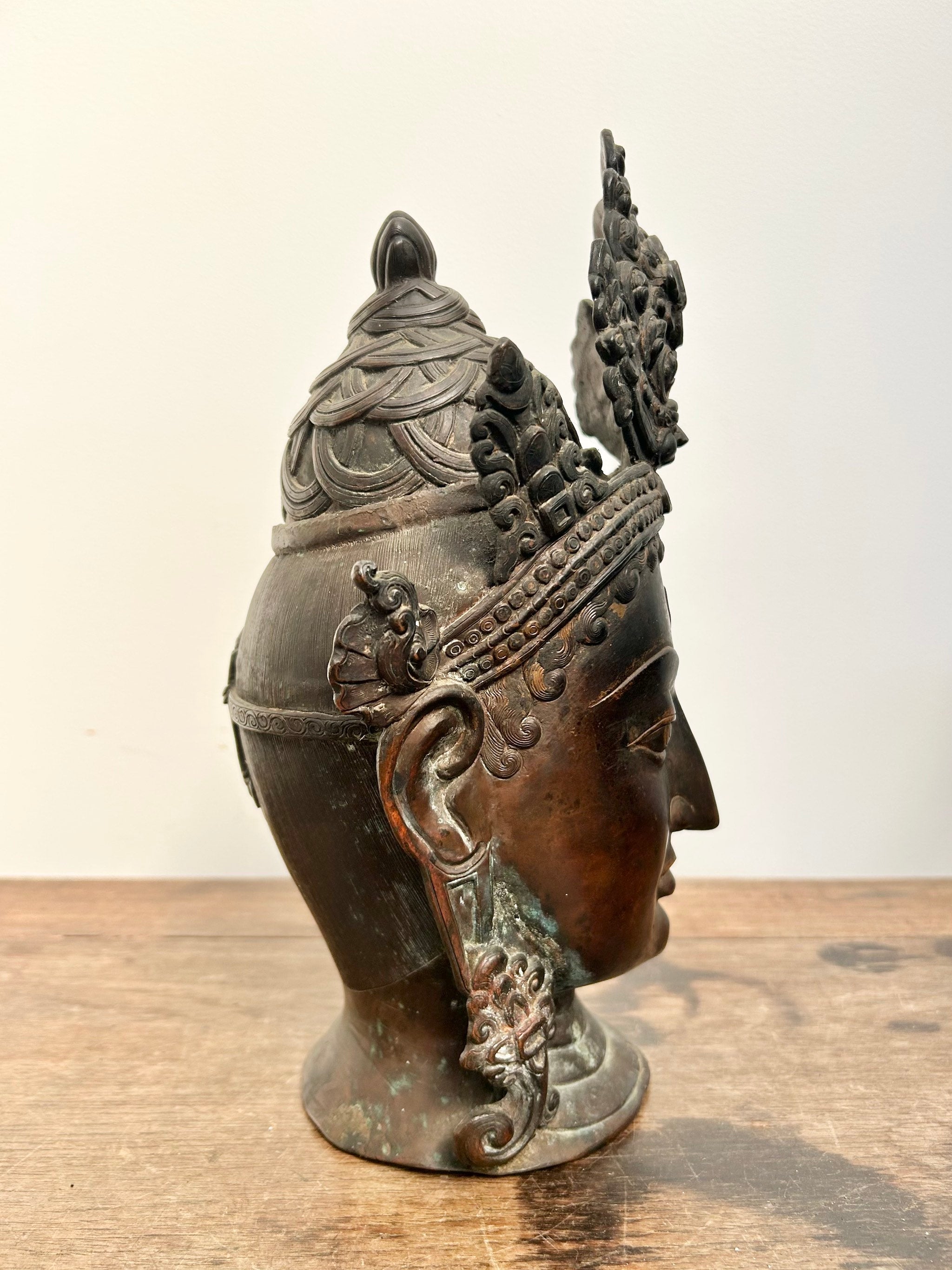 Bronze statue of Tara head with intricate details on a wooden surface