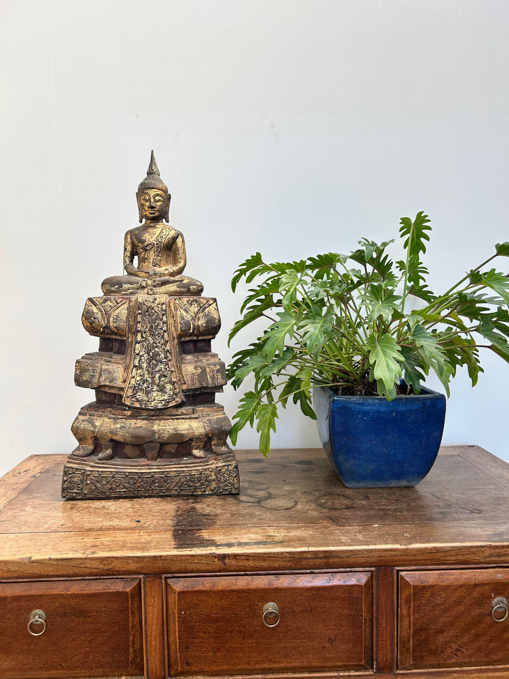 Bronze Buddha statue on a wooden cabinet with a potted plant