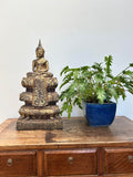 Bronze Buddha statue on a wooden cabinet with a potted plant