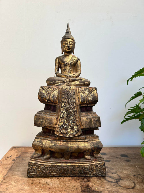 Bronze Buddha statue on a wooden surface with a white background