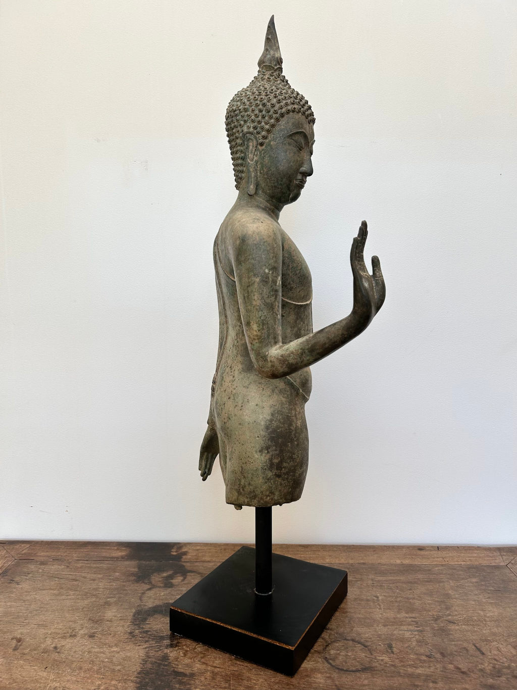 Bronze statue of a Buddha on a wooden surface with a white background