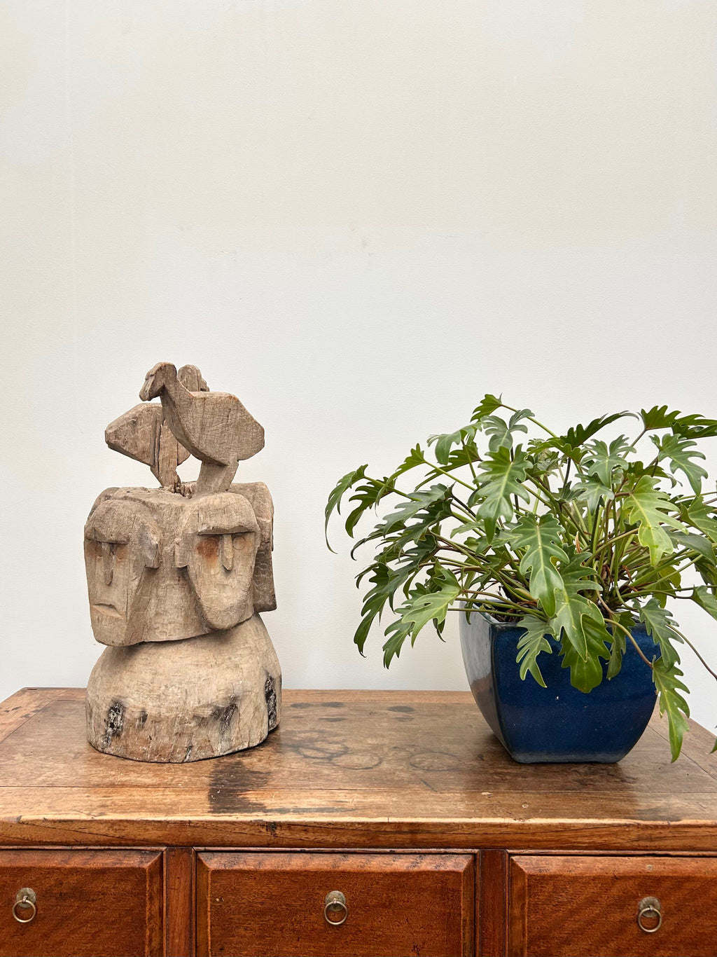 Wooden cabinet with a stone sculpture and potted plant on top against a white wall.