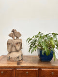 Wooden cabinet with a stone sculpture and potted plant on top against a white wall.